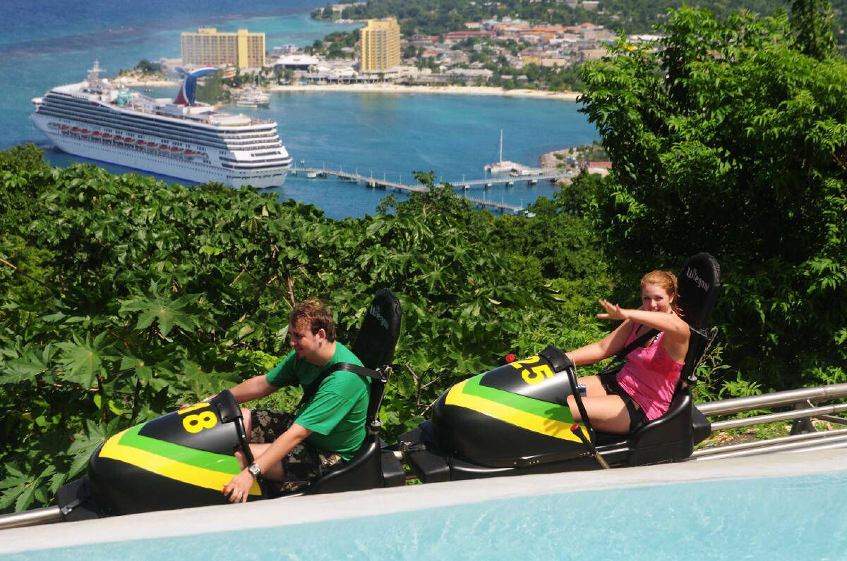 Dos personas en una atracción acuática con vistas a un crucero y un pueblo costero al fondo.