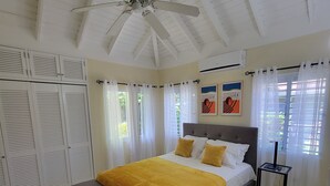 A bedroom with a bed, a grey bench, a ceiling fan, and a bedside table with a phone and a lamp. - Island Treasure Villa (St. Ann, Ocho Rios)