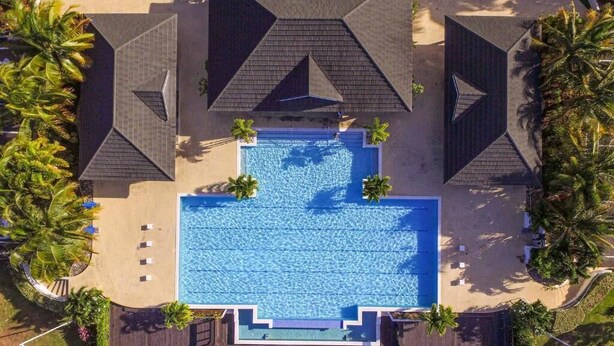 An aerial view of a resort with a central swimming pool, surrounded by palm trees and shaded by geometric roof structures. - Island Treasure Villa (St. Ann, Ocho Rios)