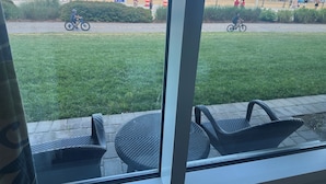 Uitzicht vanuit een raam op een strand met stoelen en een grasveld.
