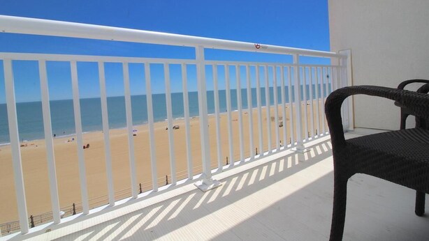 Een balkon met een witte reling dat uitkijkt over een strand.