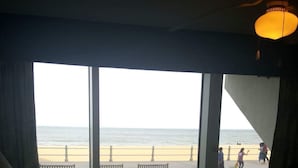 Een kamer met een groot raam met uitzicht op een strand, een bed en een lamp.