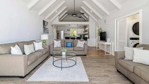 A spacious living area with a high ceiling, a ceiling fan, and a kitchen in the background. - Southampton 4BR Home | Pool, Game Room (Southampton)
