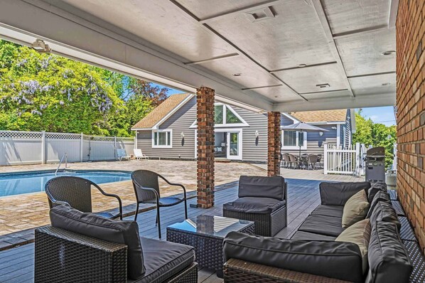 A covered outdoor area with a pool, outdoor furniture, and a brick wall.
