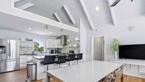 A modern kitchen with a large island, stainless steel appliances, and a dining area with a long table and chairs. - Southampton 4BR Home | Pool, Game Room (Southampton)