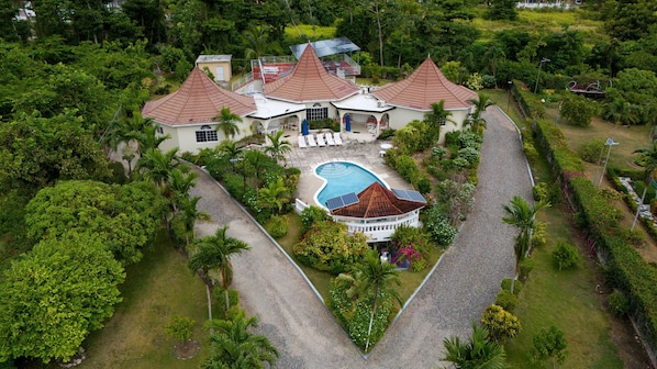 A large, multi-story building with a swimming pool, surrounded by lush greenery.