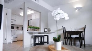 Een moderne keuken met witte kasten, een magnetron en een eethoek met een ronde tafel en stoelen.