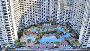 A high-rise hotel with multiple balconies, a central swimming pool, and surrounding palm trees. - Endless Views From Double Balcony! (Panama City Beach)