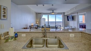 A kitchen with a double sink, a ceiling fan, and a view of the balcony. - Endless Views From Double Balcony! (Panama City Beach)