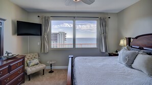 A hotel room with a bed, a chair, a dresser, a television, and a window with a view of buildings. - Endless Views From Double Balcony! (Panama City Beach)