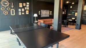 A ping pong table in a room with a dark wall, a brown leather sofa, and a table lamp. - FULL TIME LIC MGR - INDOOR/OUTDOOR PICKLEBALL - SPEAKEASY - OCEANFRONT RESORT! (Key Largo)