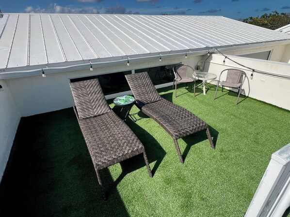 A rooftop terrace with two lounge chairs, a small table, and a chair.