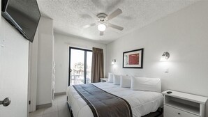 A hotel room with a bed, a nightstand, a ceiling fan, a TV, and a window with curtains.