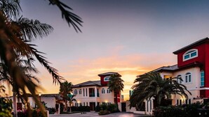 A row of modern, two-story houses with a uniform architectural style, featuring a central entrance and a well-maintained garden with palm trees. - Private Villa & Apartment with Pool in Palm Beach! (Noord)