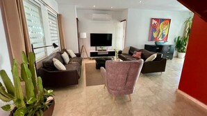 A modern living room with a sofa set, a coffee table, and a TV. There is a cactus plant and a painting on the wall. - Private Villa & Apartment with Pool in Palm Beach! (Noord)