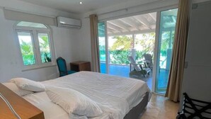 A bedroom with a large bed, a desk, and a chair. There is a sliding glass door leading to a balcony with a view of a pool. - Private Villa & Apartment with Pool in Palm Beach! (Noord)