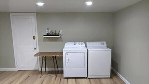 Une buanderie avec deux machines à laver blanches, un banc en bois et une porte blanche.