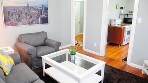 Un salon avec un canapé gris, une table basse blanche et un tableau représentant un paysage urbain accroché au mur.