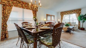 Un coin repas avec une table en bois dressée pour quatre personnes, entourée de chaises en osier agrémentées de coussins à motifs floraux.