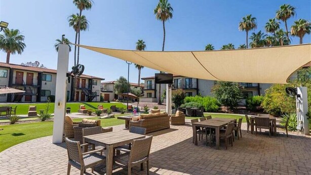 An outdoor patio area with tables and chairs, palm trees, and a building in the background. - 118 Luxury Getaway in Scottsdale | Spacious Suite, Outdoor Entertainment & Heated Pool (Scottsdale)