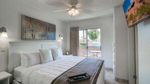 A hotel room with a bed, ceiling fan, artwork, and a view of the outdoors.