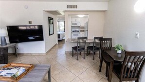 A living room with a flat-screen TV, a coffee table, and a dining area with a table and chairs.