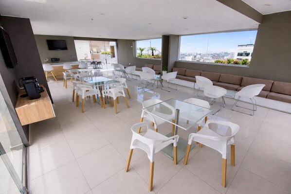A modern hotel room with a dining area, a sofa set, and a TV mounted on the wall.