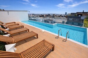 A rooftop pool with wooden loungers and a city view.