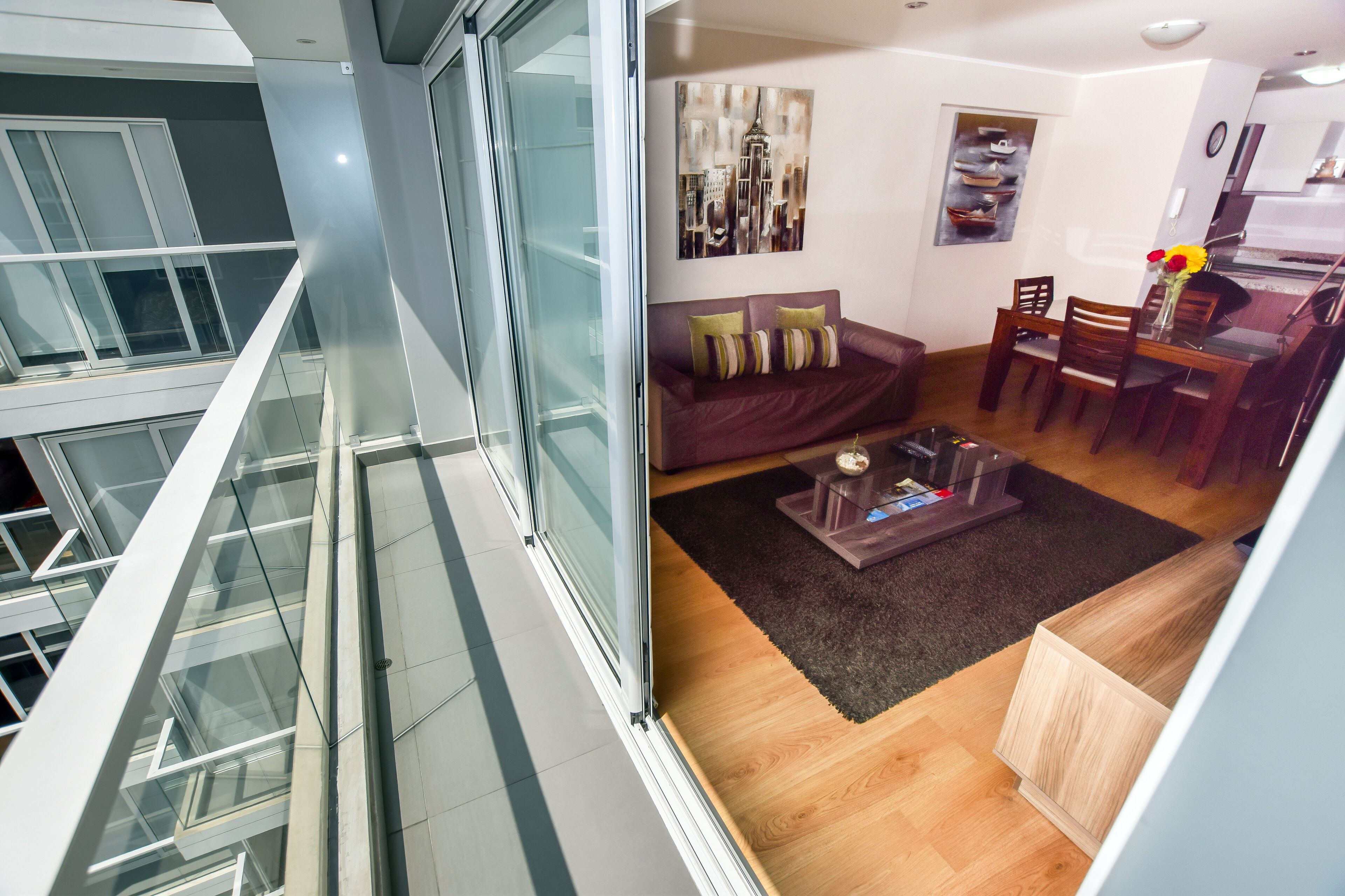 Ein modernes Interieur mit einem Glasbalkon, einem Wohnbereich mit Sofa und Couchtisch sowie einem Essbereich mit Stühlen und Tisch.