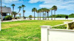 A grassy area with palm trees and a white building. - Unique Pass-a-Grille condo just steps from the sand.. (St Pete Beach)