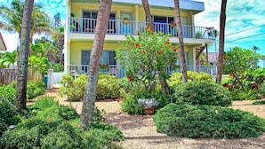 A two-story building with balconies, surrounded by lush greenery and palm trees. - Unique Pass-a-Grille condo just steps from the sand.. (St Pete Beach)