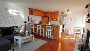 A modern living room with a dark sofa, a coffee table, and a kitchen area with wooden cabinets and a bar stool. - Unique Pass-a-Grille condo just steps from the sand.. (St Pete Beach)