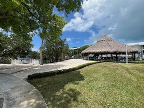 A beachside resort with a thatched-roof pavilion, a pool, and a well-maintained lawn.
