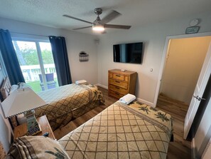 Una habitación de hotel con dos camas, ventilador de techo, televisión, cómoda y una puerta.