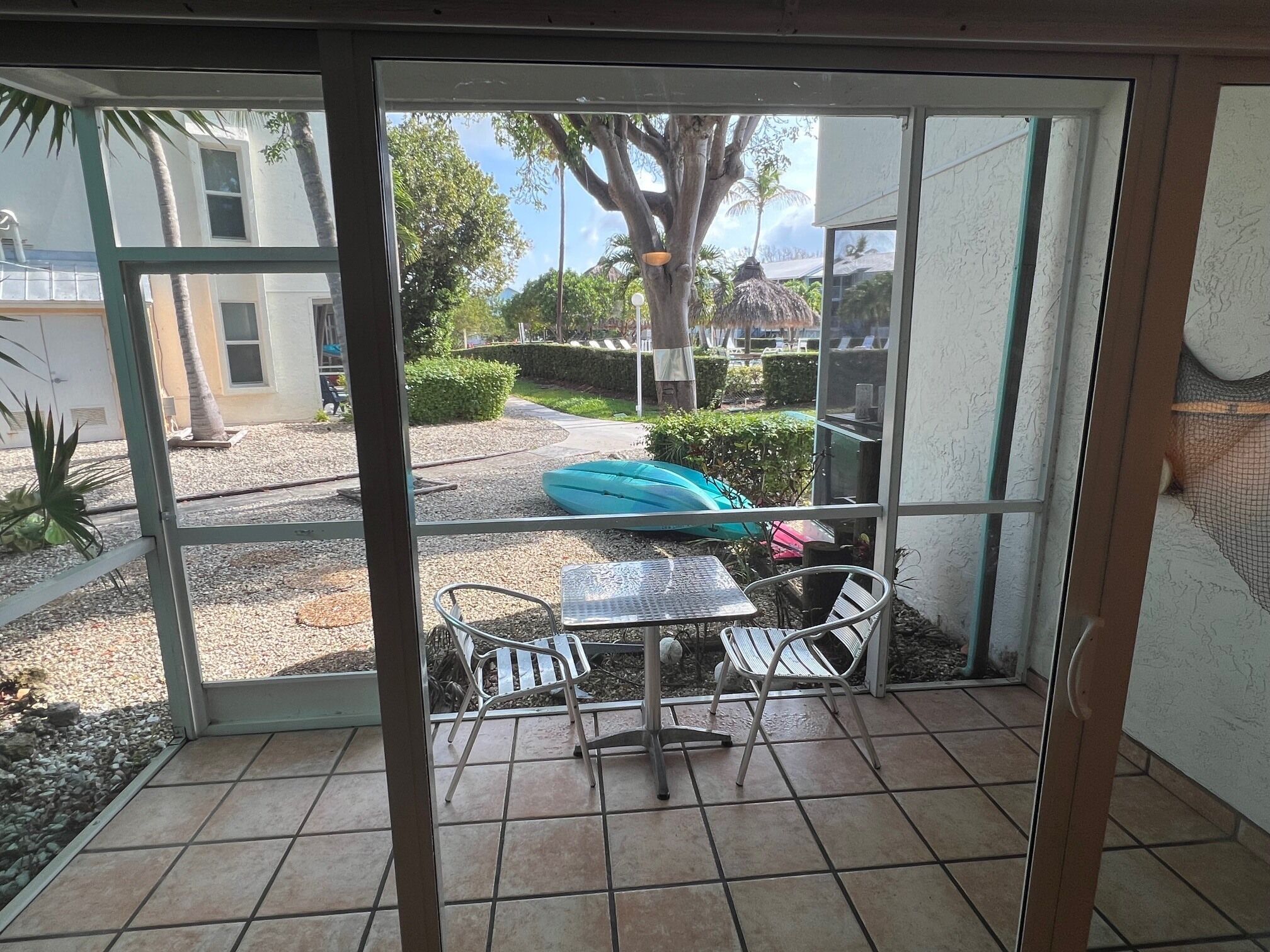 A room with a glass door, a tiled floor, a metal table, and two metal chairs.