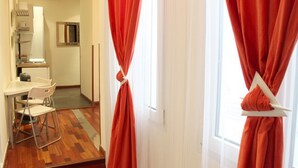 Hotellihuone, jossa on puulattia, valkoinen työpöytä tuolilla ja punaiset verhot.