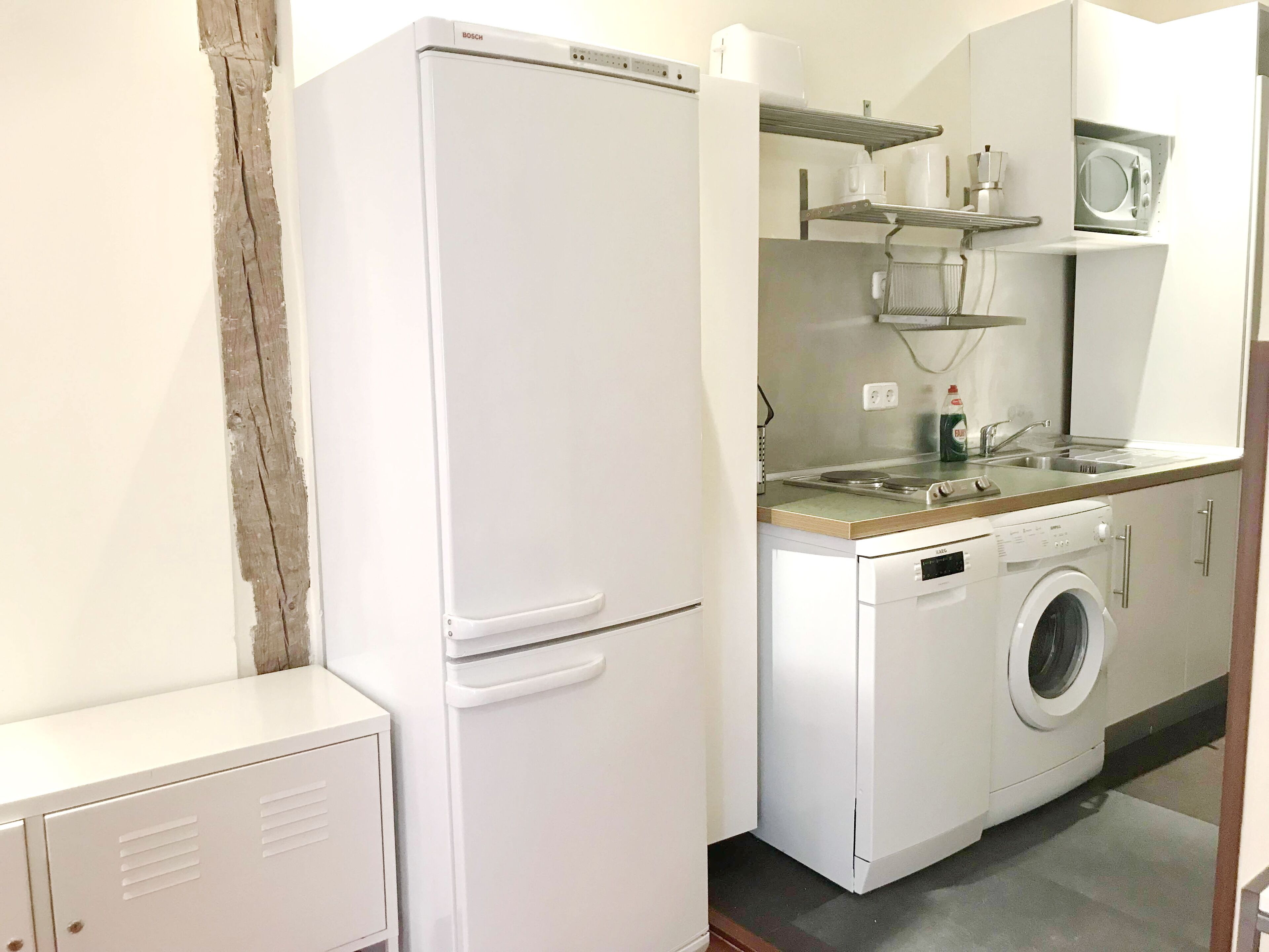 Une cuisine compacte équipée d’un réfrigérateur Bosch, d’un lave-linge et d’un four à micro-ondes, le tout installé sur un plan de travail.