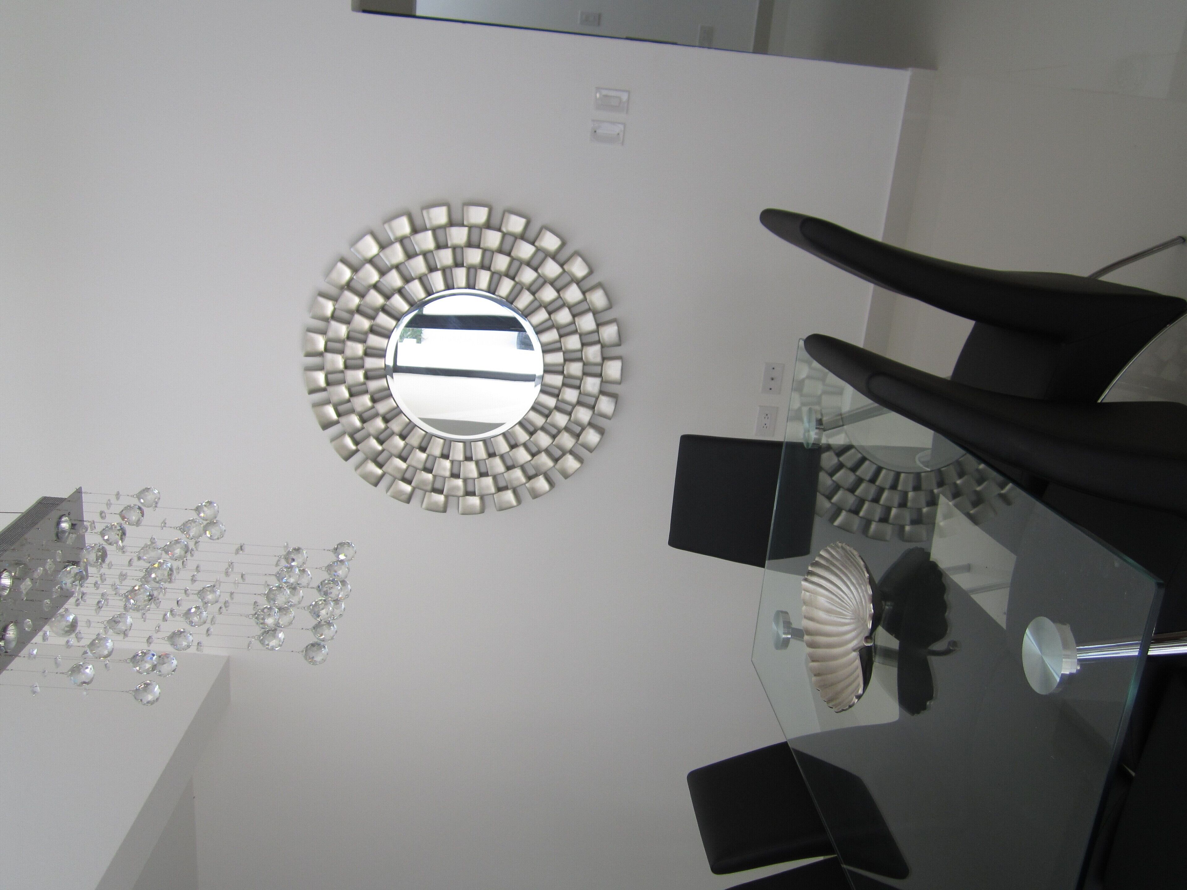 Een modern interieur met een ronde spiegel, zwarte stoelen en een glazen tafel.