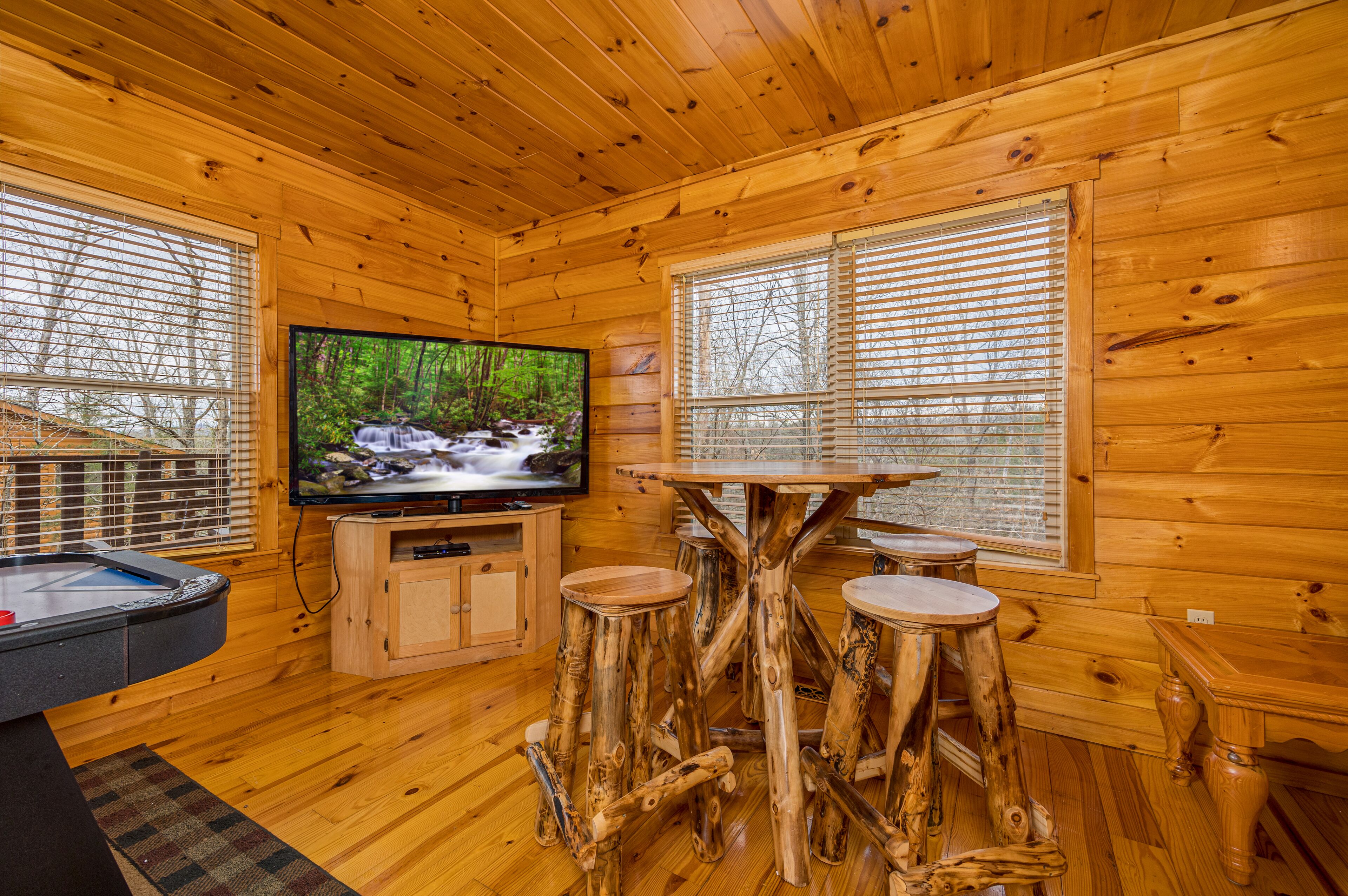 Een houten cabin met een televisie, houten krukken en een tafel.