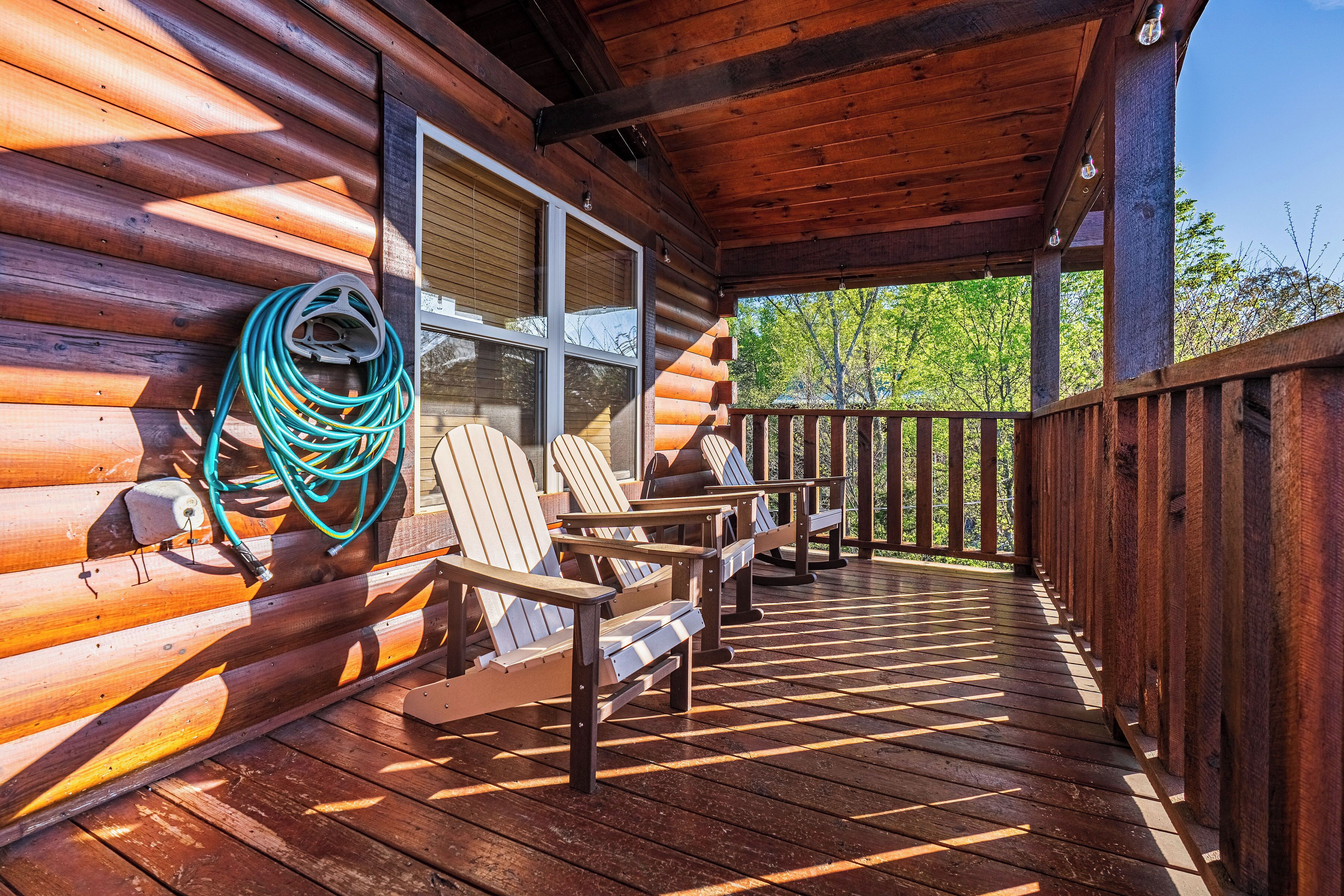 A wooden deck with Adirondack chairs and a coiled garden hose.