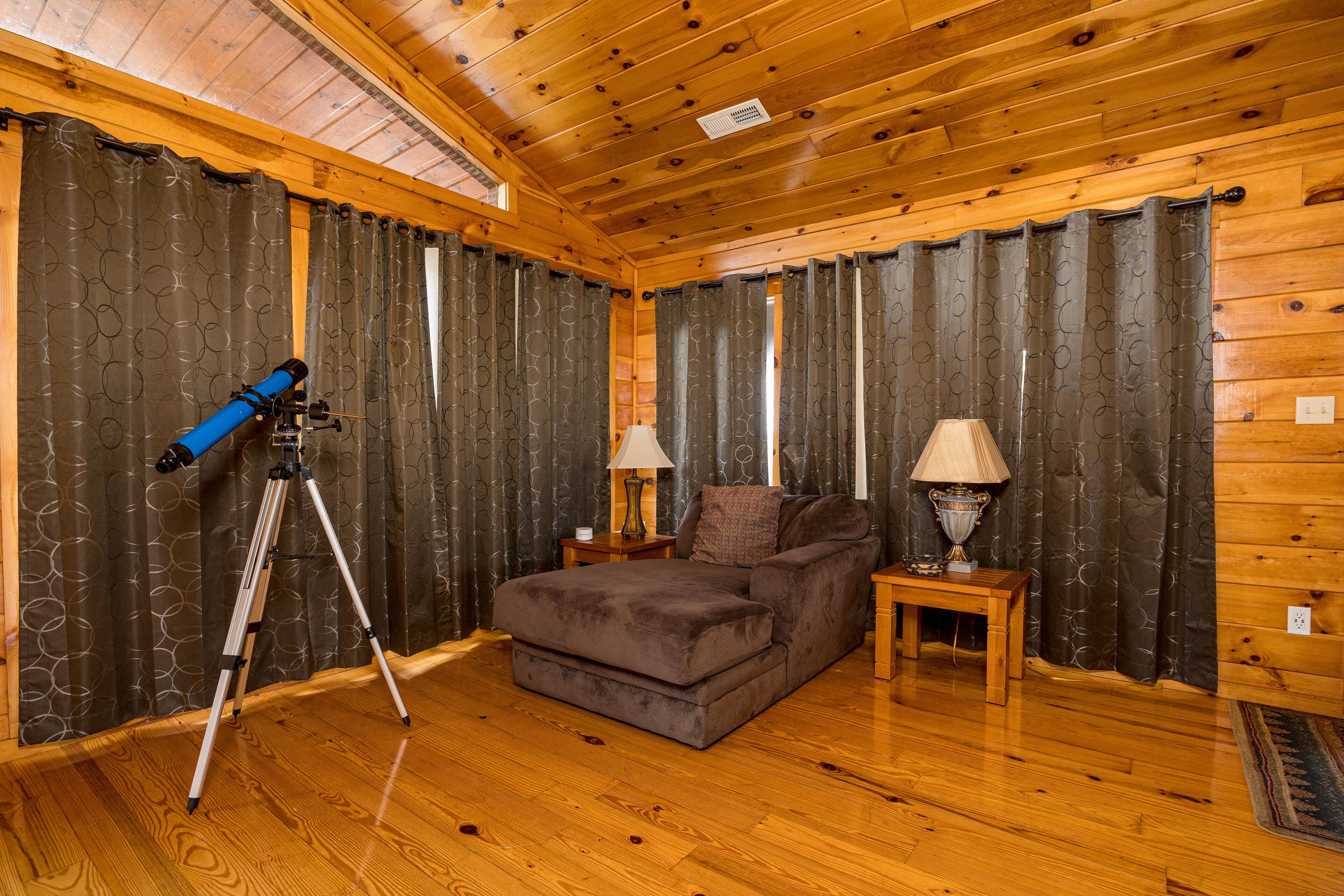 L’intérieur d’un chalet accueillant, avec un plafond en bois, un canapé, deux lampes et un télescope monté sur un trépied.