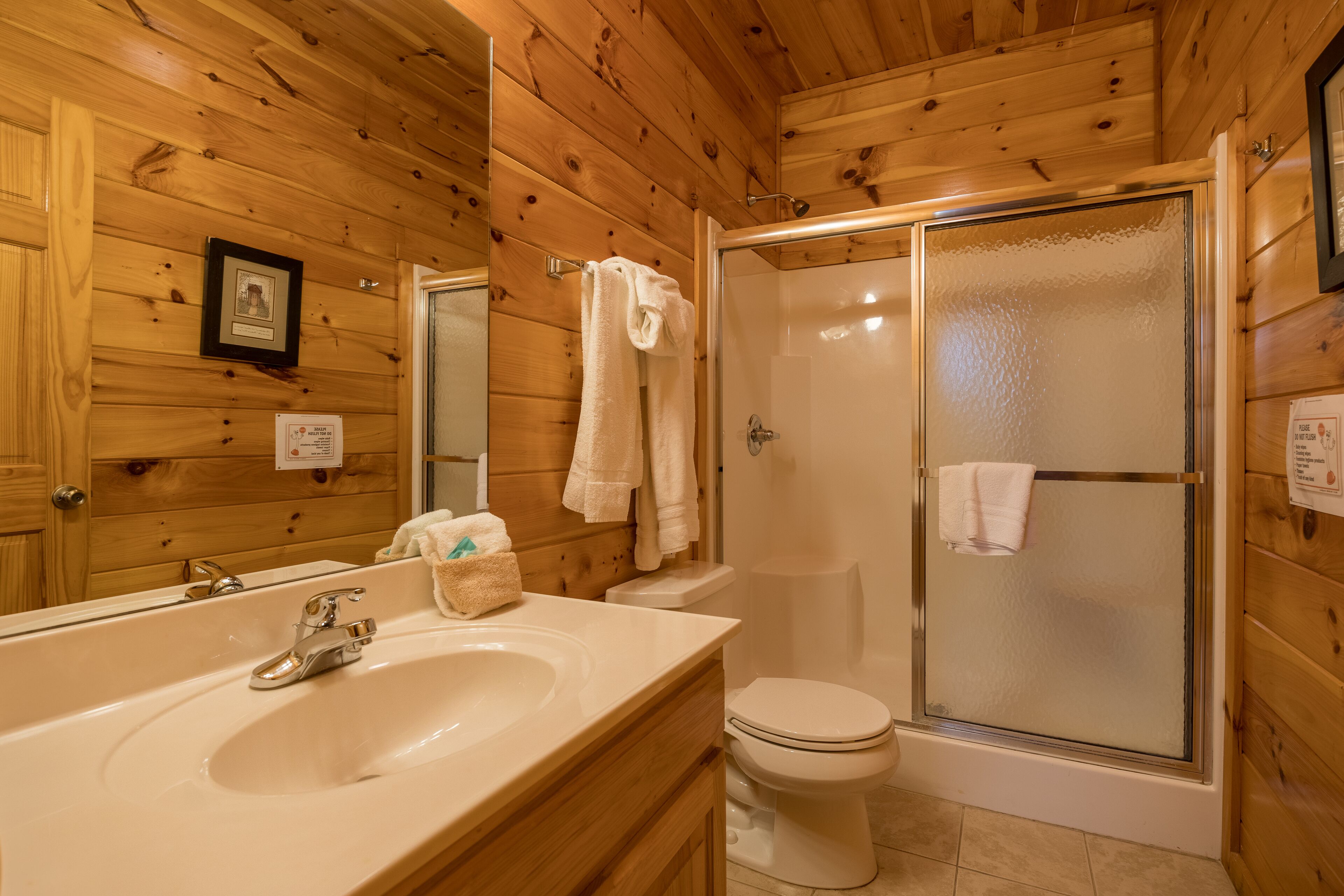 A wooden-paneled bathroom with a sink, toilet, and glass-enclosed shower.