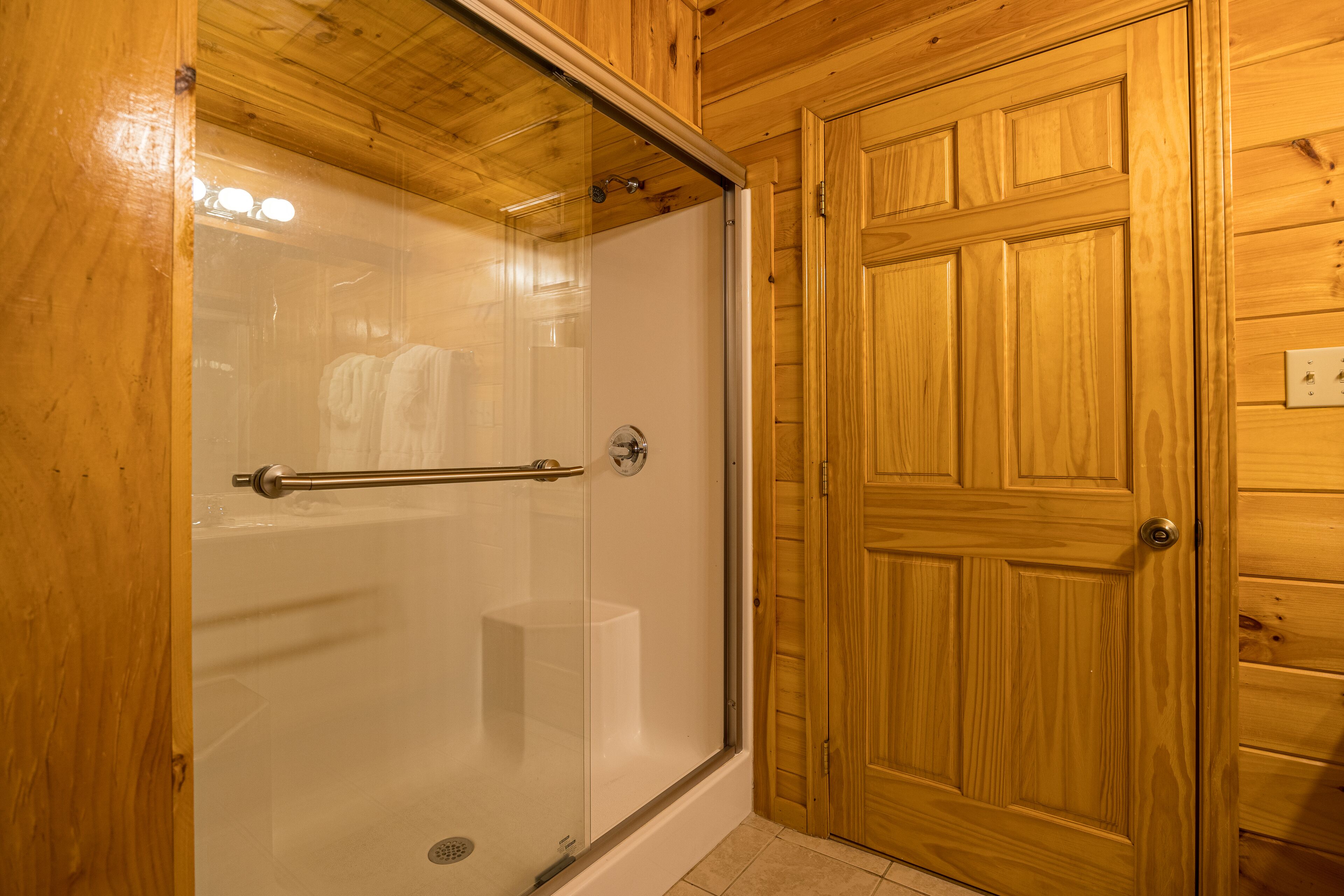 Ein Badezimmer mit Holzwänden, einer Glaskabine für die Dusche und einer Holztür.