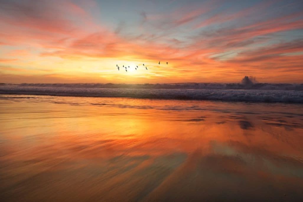 A beach at sunset with a calm sea and a clear sky.