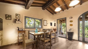 A dining area with a wooden table and chairs, a window with a view of greenery, and a kitchen area with cabinets and a stove. - Villa in Toscana - Reggello con Piscina, Wi-Fi, Giardini.  (Reggello)
