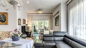 Een woonkamer met een zwarte leren bank, een glazen salontafel, een kroonluchter en een schilderij aan de muur.