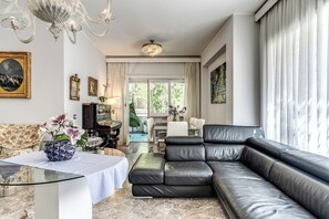 Een woonkamer met een zwarte leren bank, een glazen salontafel, een kroonluchter en een schilderij aan de muur.