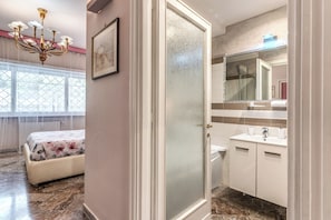 Un dormitorio con cama, una lámpara de araña, una ventana y un baño con lavamanos y espejo.