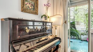 Een vleugelpiano in een goed verlichte kamer met uitzicht op een tuin door een glazen deur.