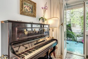 Een vleugelpiano in een goed verlichte kamer met uitzicht op een tuin door een glazen deur.